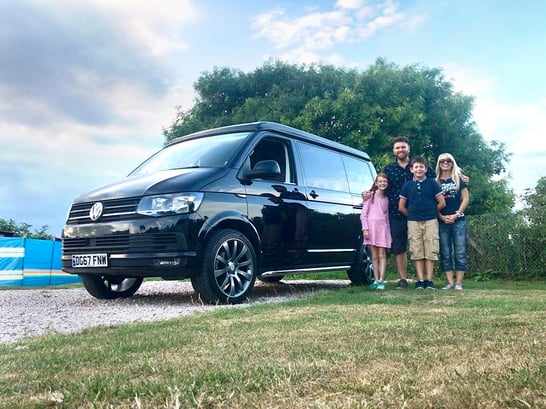 family of four posing in front of a campervan in a campsite