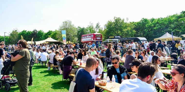 photo of a festival food court, filled with people sitting on benches on a sunny day
