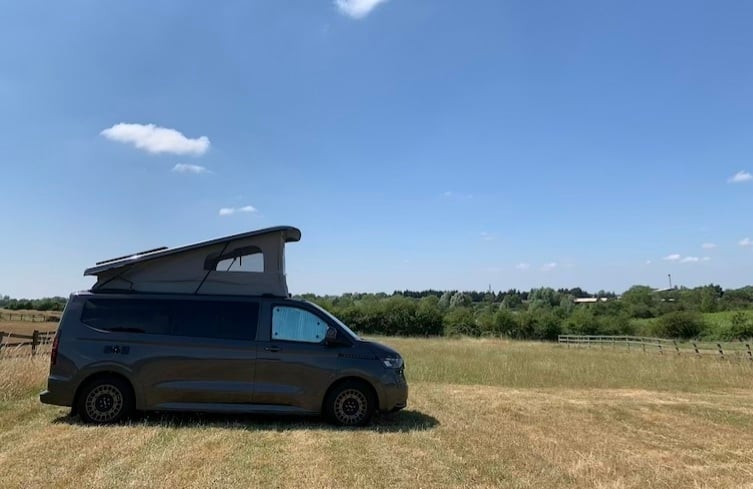 Grey CamperKing T7 Freedom with off-road wheels parked sideways in an open field, showing dry grass and a clear blue sky on a summers day