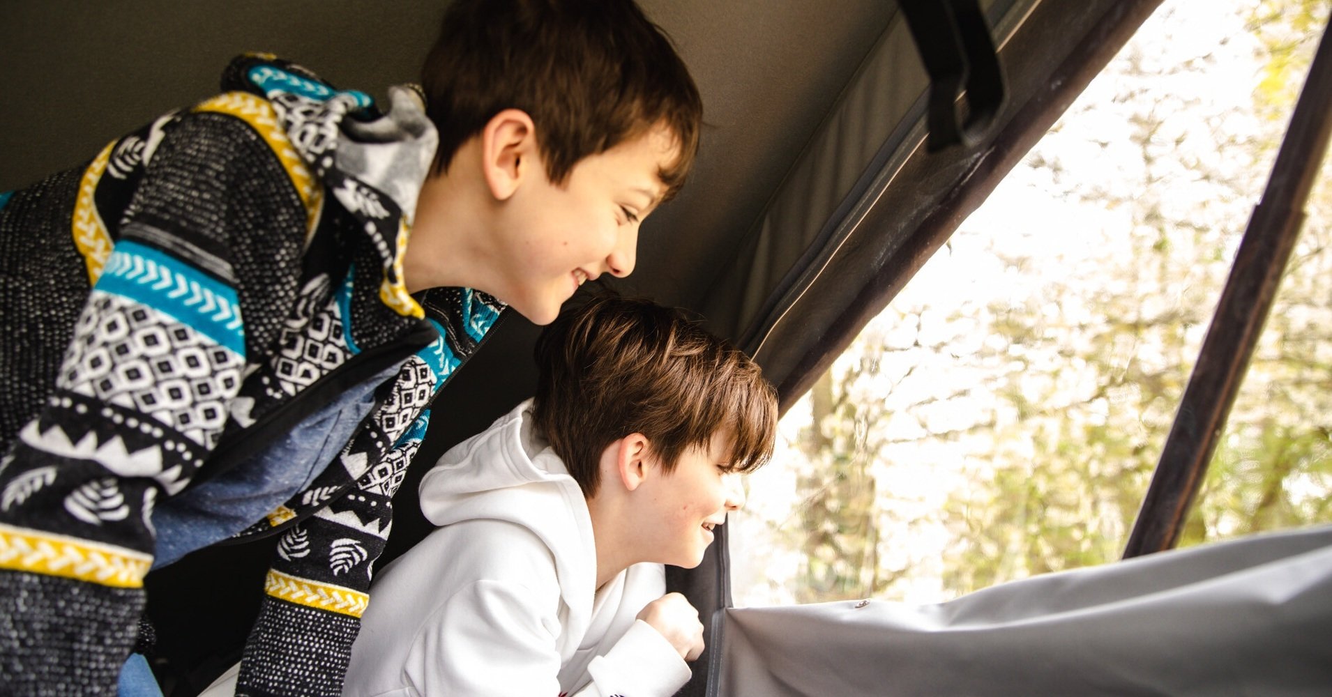 children in a pop top bed, looking out of the window smiling